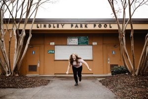 woman laughing and running in front of Lindley Park Pool building during day